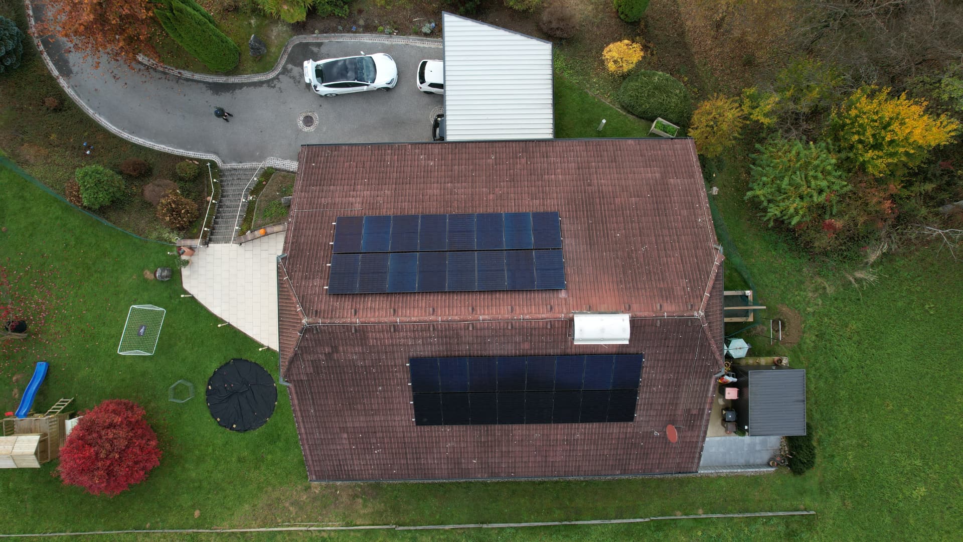 Luftaufnahme eines Wohnhauses mit rotem Ziegeldach und zwei Feldern schwarzer Photovoltaik-Module